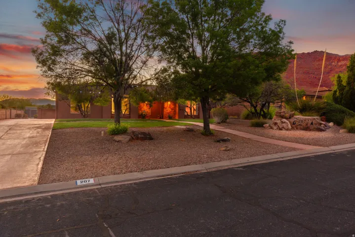 Southwestern-style home featuring a stucco exterior, expansive gravel landscaping, mature trees, and a concrete driveway