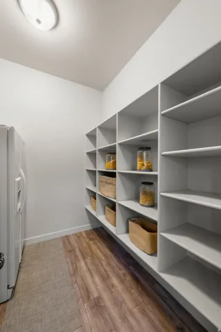 Spacious pantry featuring extensive built-in shelving, wood-finish flooring, and recessed ceiling lighting