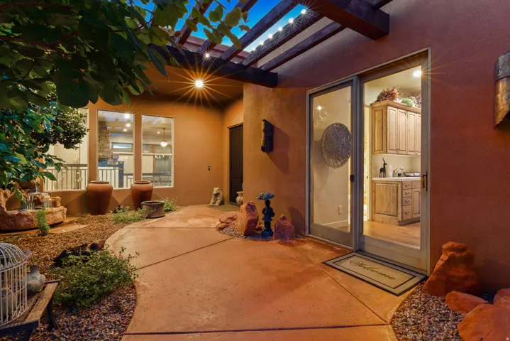 Outdoor patio featuring a wooden pergola with string lighting, a concrete pathway, and a stone water feature