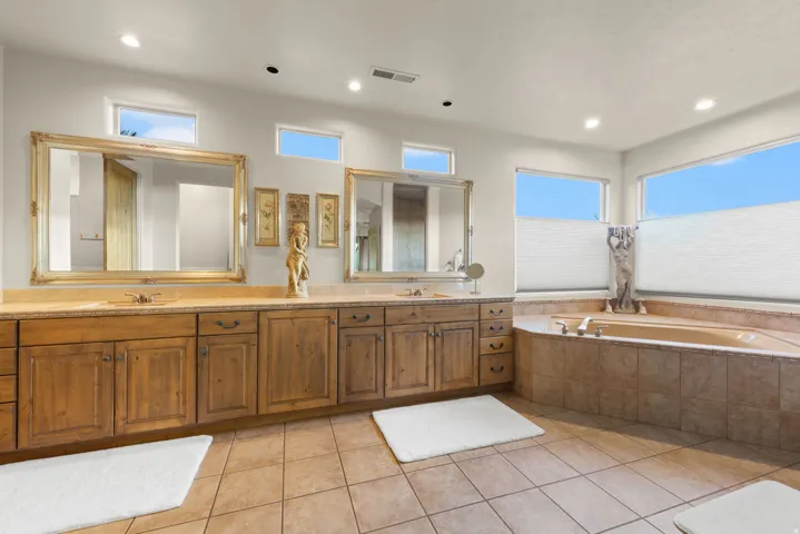 Expansive bathroom featuring a double vanity with wood cabinetry and light-colored countertops, a built-in corner bathtub, and multiple windows