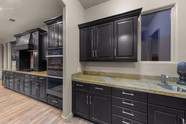 Kitchen featuring dark cabinetry, lighter wood-finish flooring, built-in oven, built-in microwave, and stone countertops