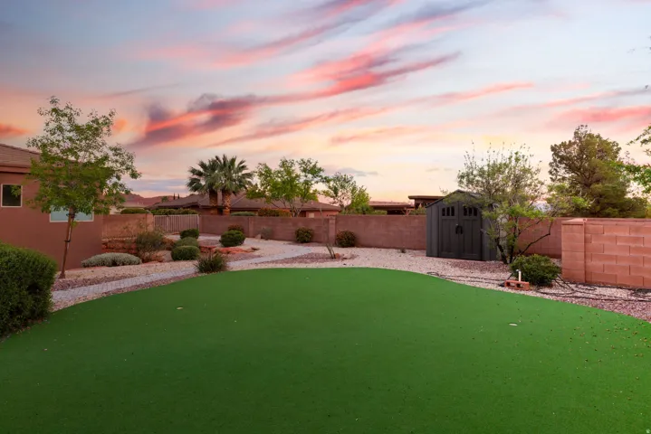 Backyard featuring a green turf area, gravel ground cover, mature desert landscaping, and a privacy wall