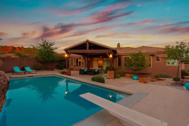 Backyard oasis featuring a swimming pool with diving board, expansive concrete patio, and a covered pergola