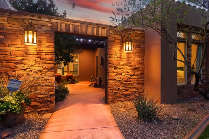 Stone entry archway with integrated sconce lighting, showcasing a paved pathway and xeriscape landscaping