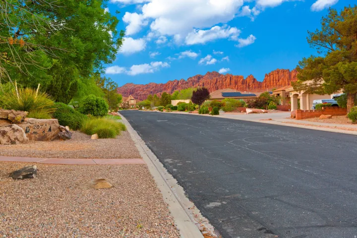 Paved street with a gravel and stone-lined verge, featuring established landscaping and mature trees