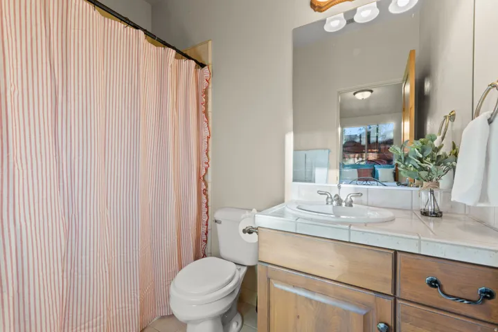 Bathroom featuring a wood-finish vanity with dark hardware, a tile countertop, and an integrated sink with a chrome faucet