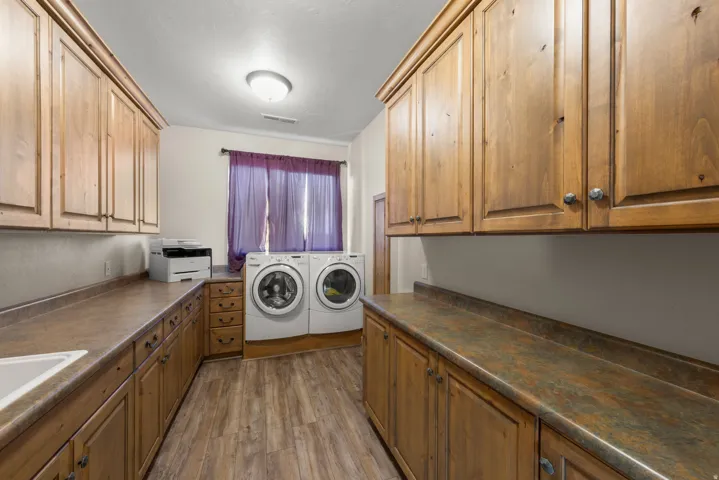 Dedicated laundry room featuring wood-finish flooring, extensive wood cabinetry, and ample counter space