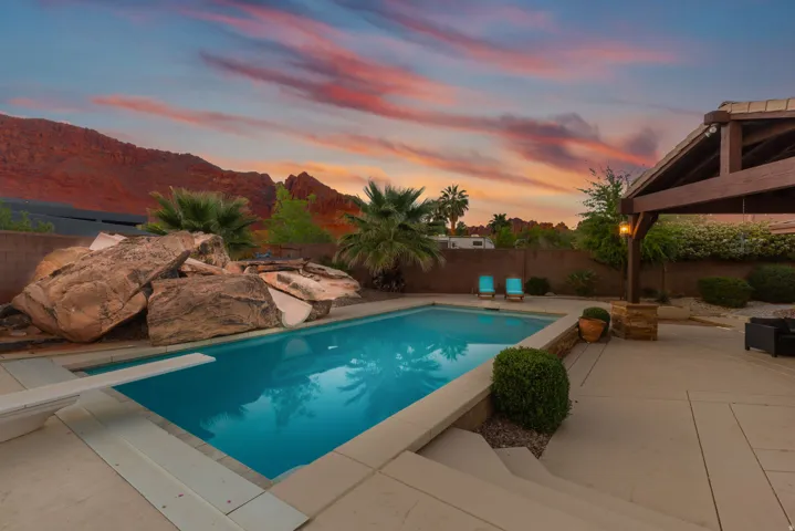 Backyard oasis featuring a swimming pool with a diving board, natural rock landscaping, and a covered patio structure