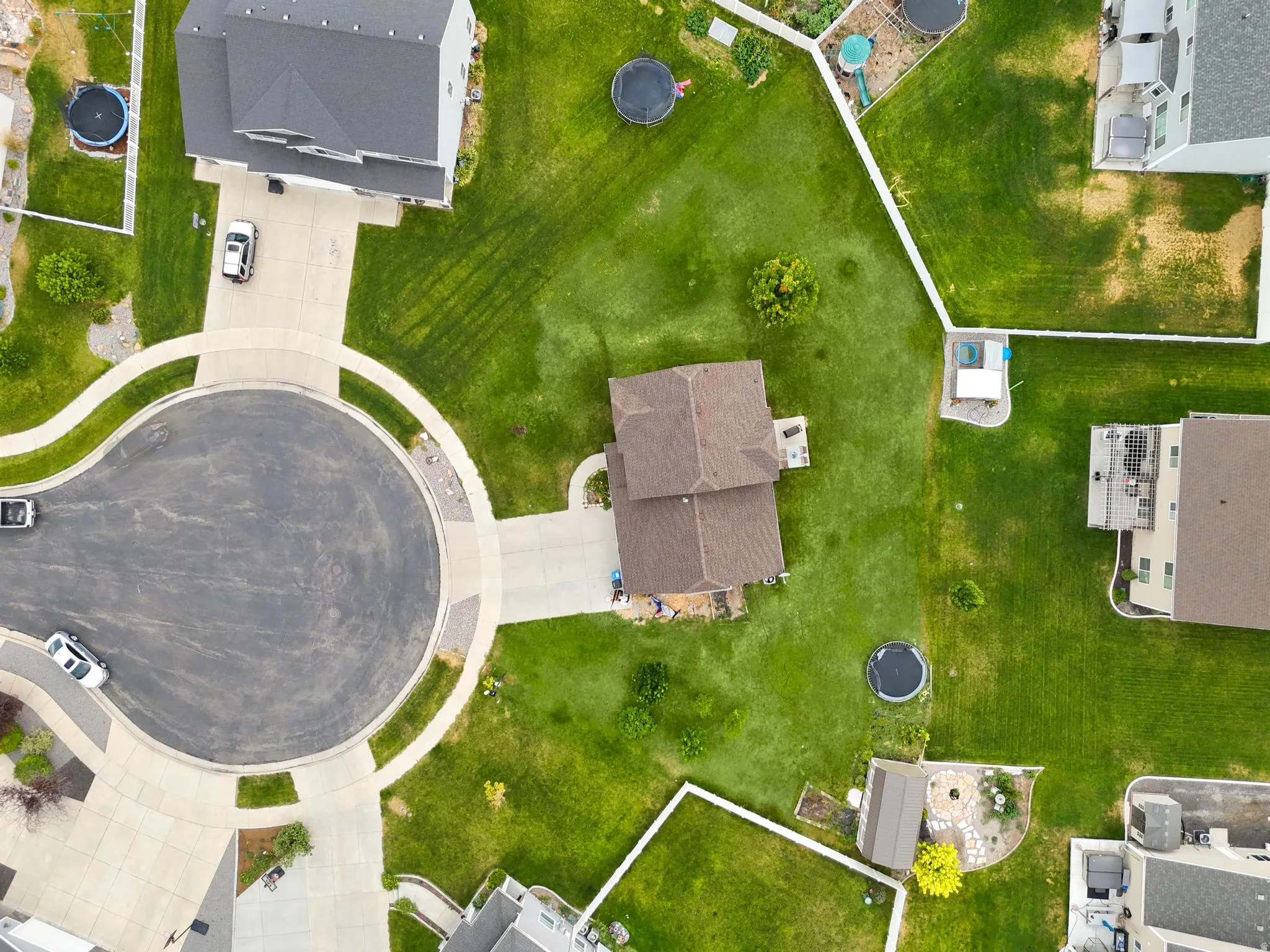Central property featuring a brown shingle roof, paved driveway, and expansive lawn