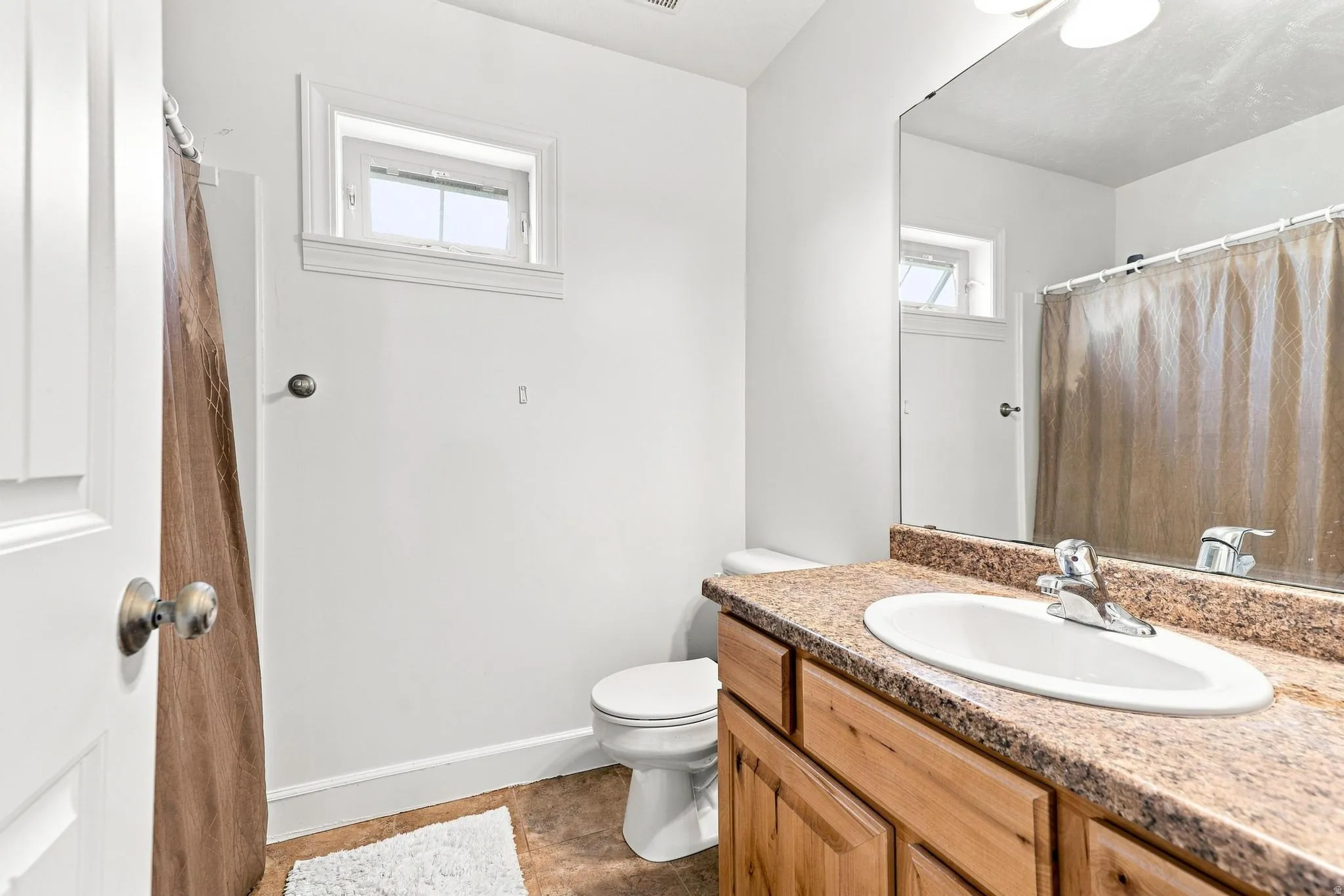 Primary Bathroom featuring a wood-finish vanity with a speckled countertop, an integrated sink, a chrome faucet, and a wall-mounted mirror