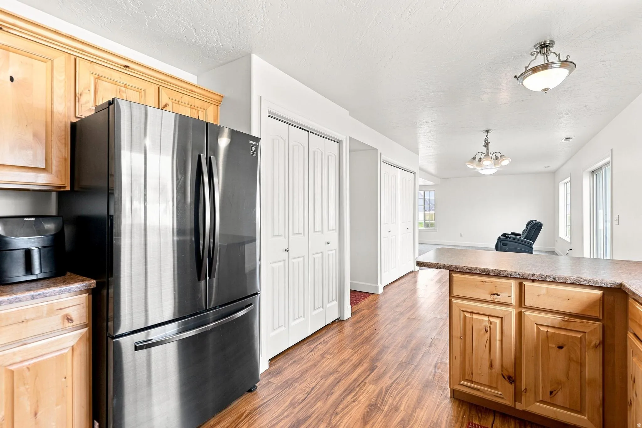 Kitchen with natural wood cabinetry, stainless steel refrigerator, and wood-finish flooring