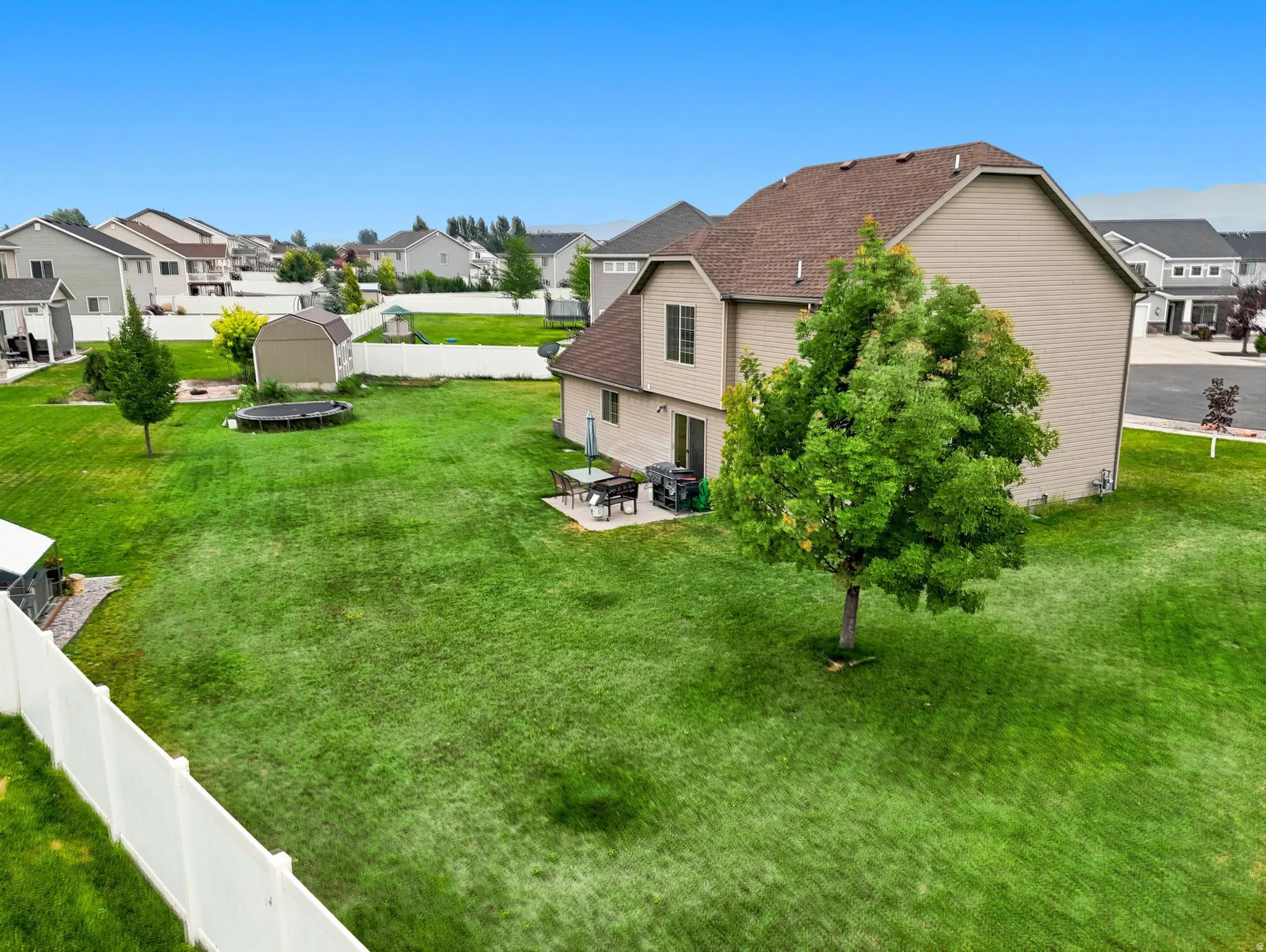 Expansive rear yard featuring a large green lawn, perimeter fencing, mature trees, and a patio area