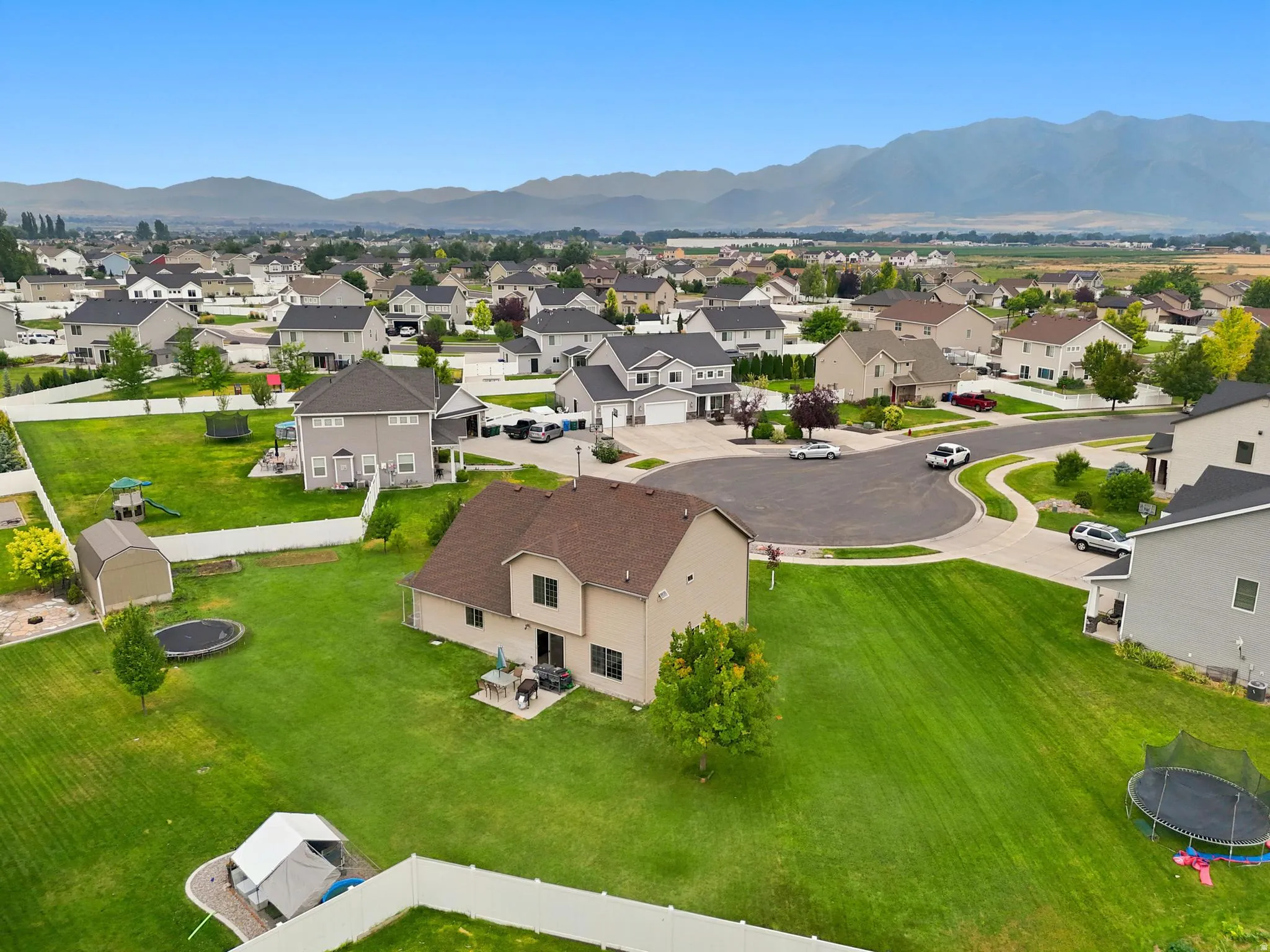 Expansive backyard with a manicured lawn, established trees, and mountainous backdrop