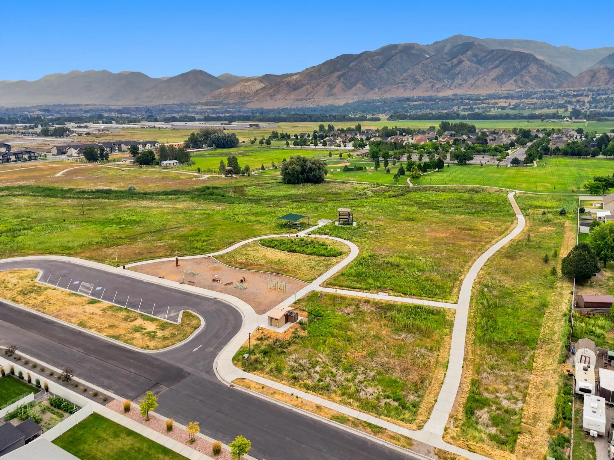 Firefly Park. Expansive green space featuring a paved path system, mountain backdrop, and distant residential areas