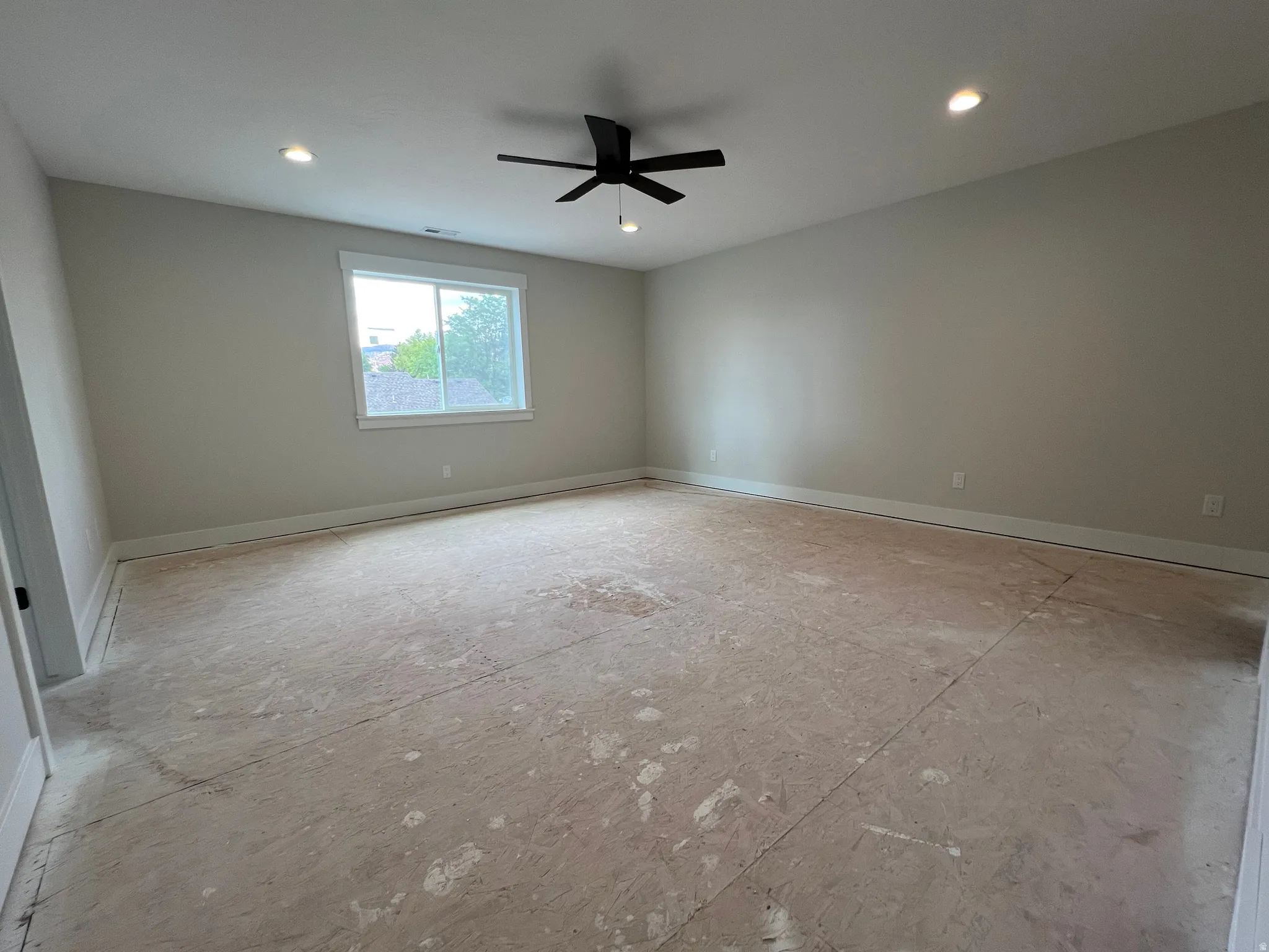 Spacious room featuring neutral painted walls, a large window with white trim, and a black ceiling fan