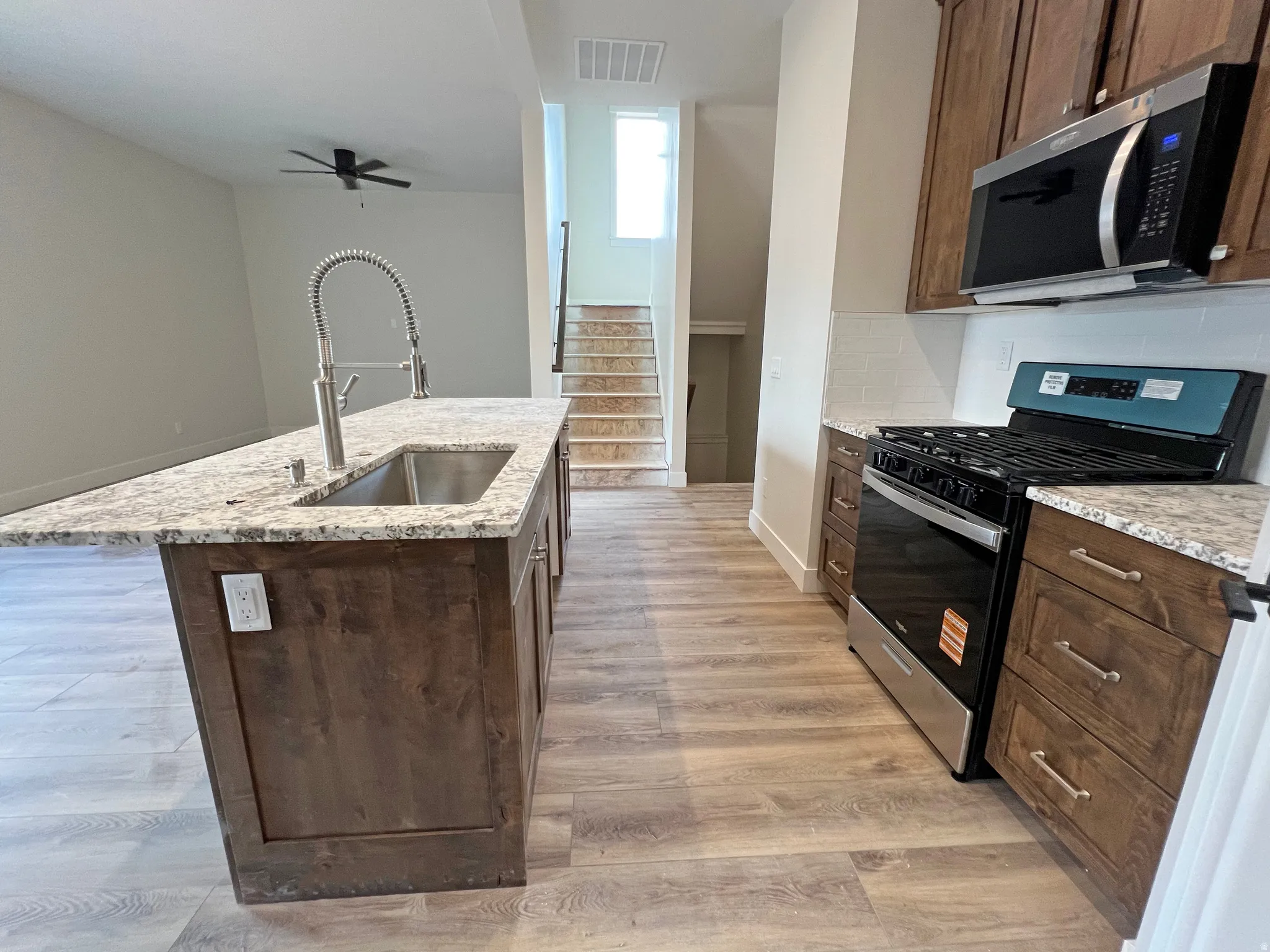 Kitchen featuring wood-finish flooring, wood cabinetry with brushed nickel hardware, light-toned stone countertops, and a subway tile backsplash