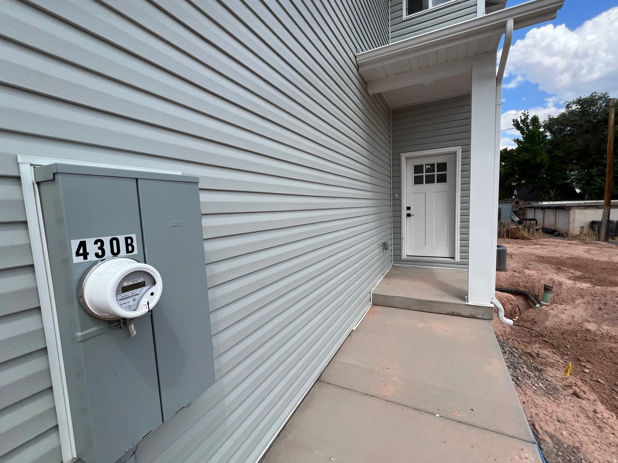 Light gray horizontal siding exterior featuring a white paneled entry door with windowpanes, a white support column, and a concrete walkway