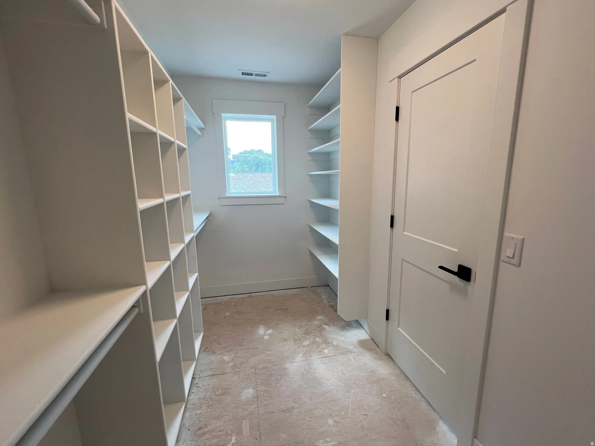 Walk-in closet featuring extensive built-in shelving, a natural light window, a modern two-panel door with matte black hardware, and light-toned flooring