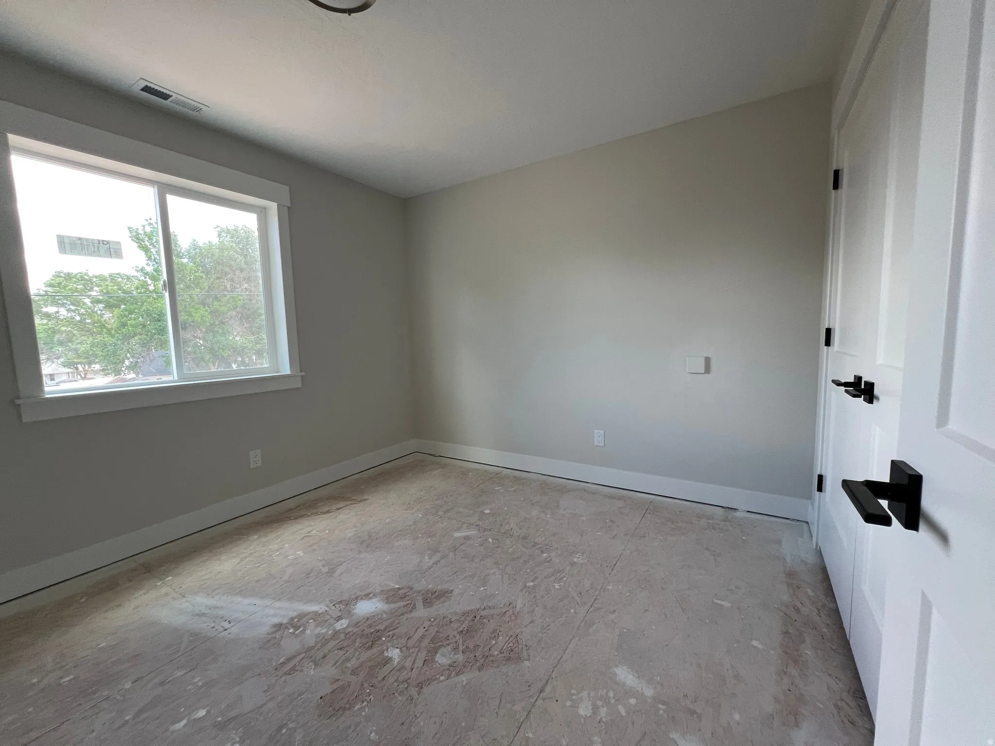 Room featuring a window with white trim, light gray walls, white baseboards, and two paneled doors with black hardware