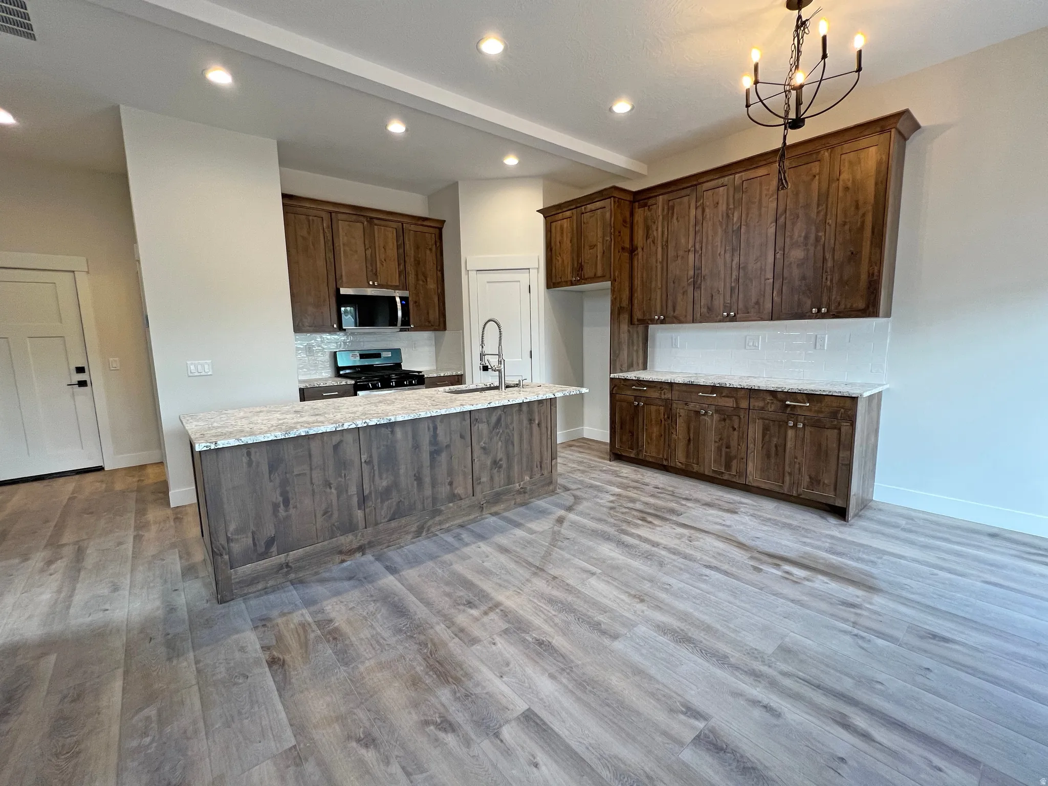 Open-concept kitchen featuring wood-finish cabinetry, light-toned countertops, a central island with integrated sink, stainless steel appliances, and wood-finish flooring