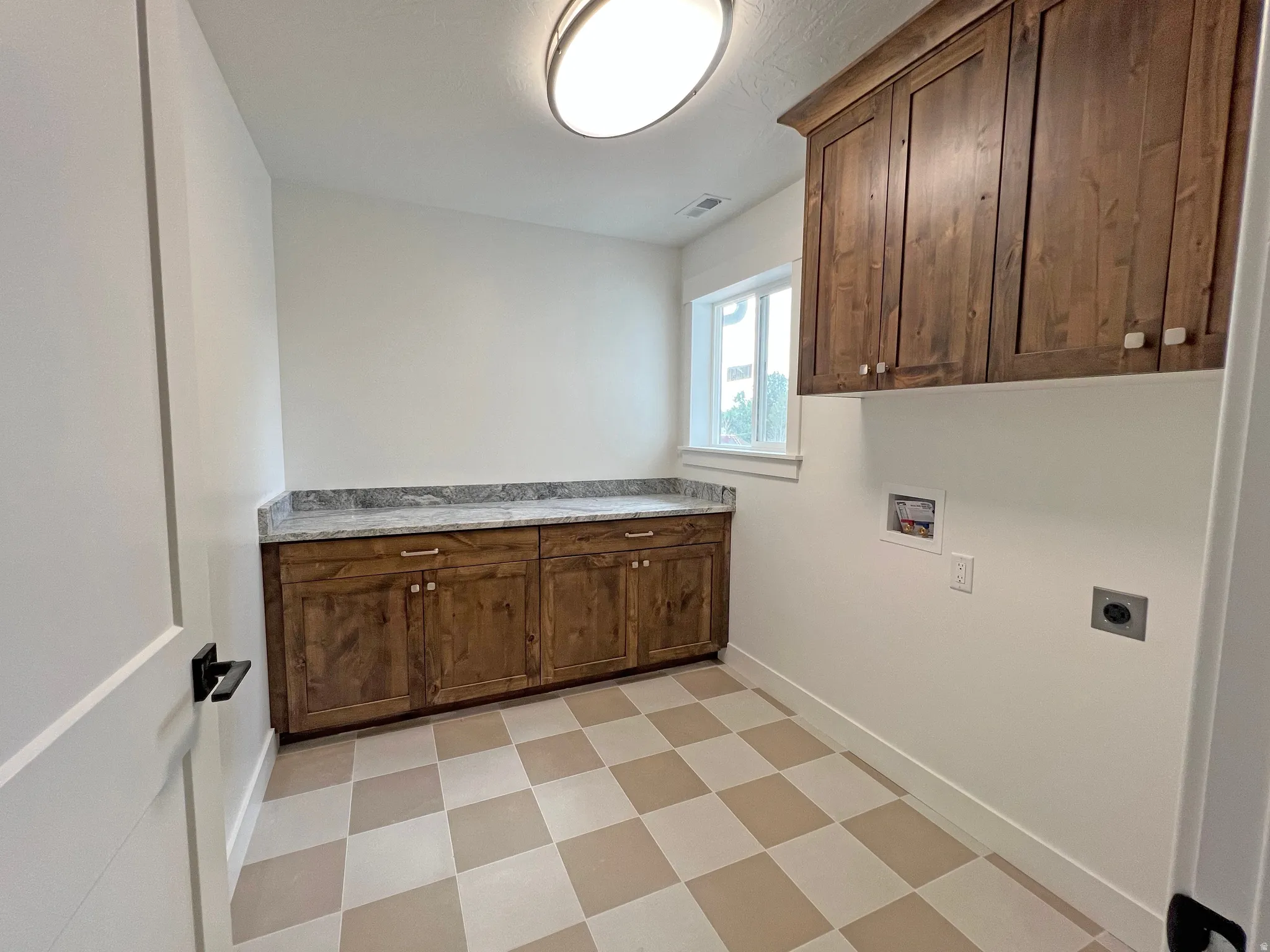 Laundry area featuring a checkered floor, built-in wooden cabinetry, granite-finish countertop, and a window for natural light