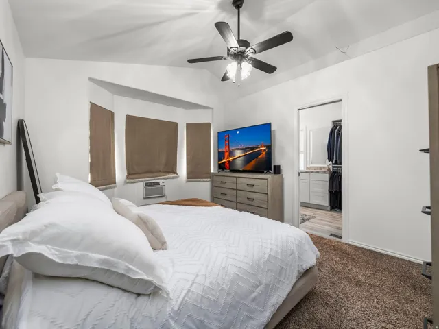 Bedroom featuring a vaulted ceiling with a ceiling fan, a bay window with natural light, and plush carpeting