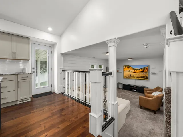 Hardwood flooring extending to a kitchen area with gray cabinetry, a tile backsplash, and a glass-paneled exterior door
