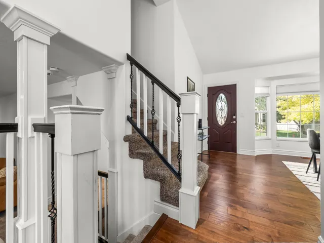 Entryway featuring wood-finish flooring, a dark wood front door with an oval leaded glass insert, and a staircase with white newel posts, white balusters, and black wrought iron detailing
