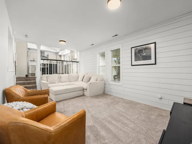 Lower-level living area featuring neutral carpeting, white shiplap accent wall, and multiple windows with blinds