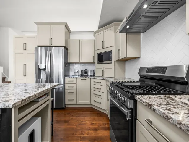 Kitchen featuring stainless steel appliances, light-toned cabinetry, wood-finish flooring, granite countertops, and a white subway tile backsplash