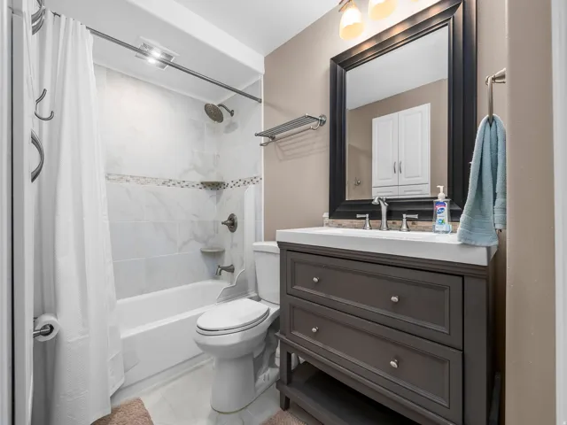 Full bathroom featuring a white tub and shower with tile surround, a dark wood vanity with a white countertop, and a framed mirror