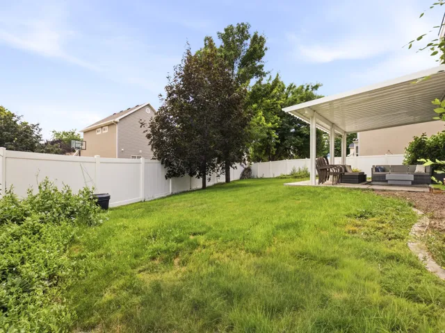 Expansive backyard featuring a spacious covered patio, a manicured lawn, mature trees, and a privacy fence