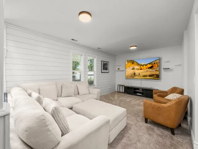 Carpeted living space featuring shiplap accent wall, built-in media console, ceiling-mounted lighting fixtures, and natural light from multiple windows