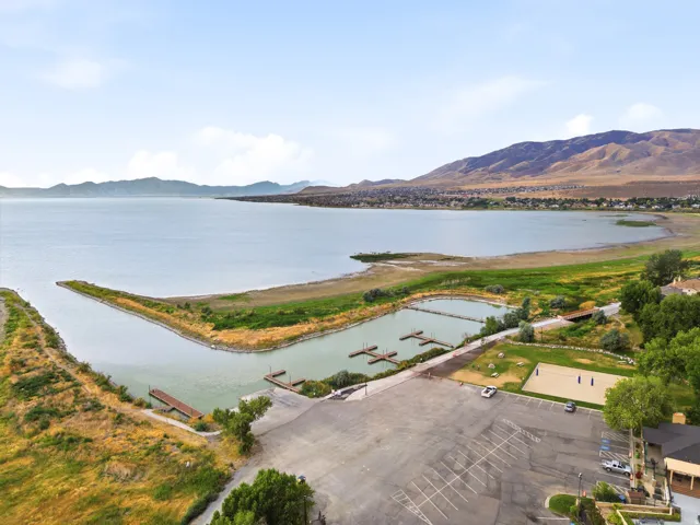 Expansive lakefront setting featuring a large parking area, multiple boat docks, a sandy sports court, and surrounding natural landscapes