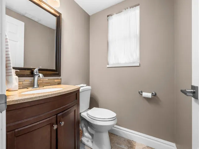 Contemporary powder room featuring a curved wood-finish vanity with a light-colored countertop and a rectangular sink