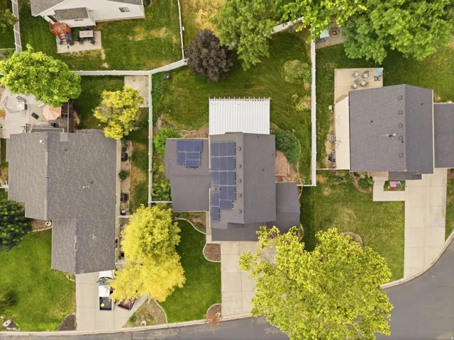 Property featuring a dark shingle roof with solar panels, a fenced backyard, and mature trees