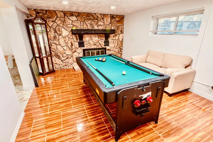 Recreation room featuring a stone-clad fireplace with a dark wood mantel, wood-finish tile flooring, recessed lighting, and a hopper window