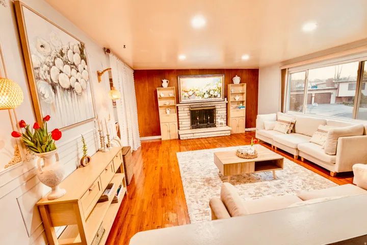Spacious living area featuring wood-finish flooring, a stone fireplace with a wood-paneled accent wall, and recessed lighting