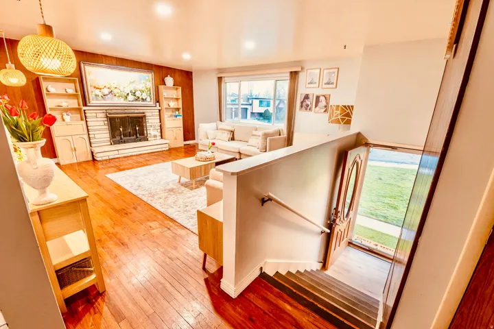 Living area featuring warm wood-finish flooring, a stone-clad fireplace with built-in cabinetry, recessed lighting, and a large front window