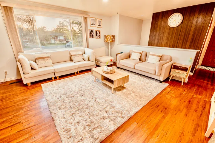Living area featuring warm wood-finish flooring, a large picture window, and a wood-paneled accent wall