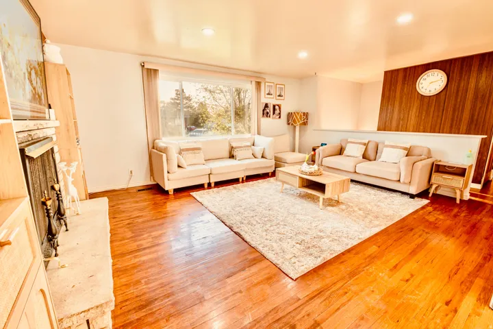 Spacious living area featuring polished wood-finish flooring, a stone fireplace with a built-in mantel, and recessed lighting