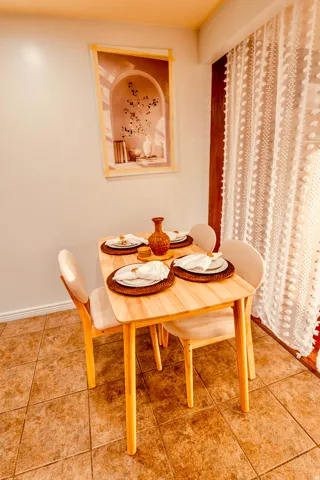 Dining area featuring warm-toned floor tiling, a light wood-finish table, and a contemporary framed wall art piece