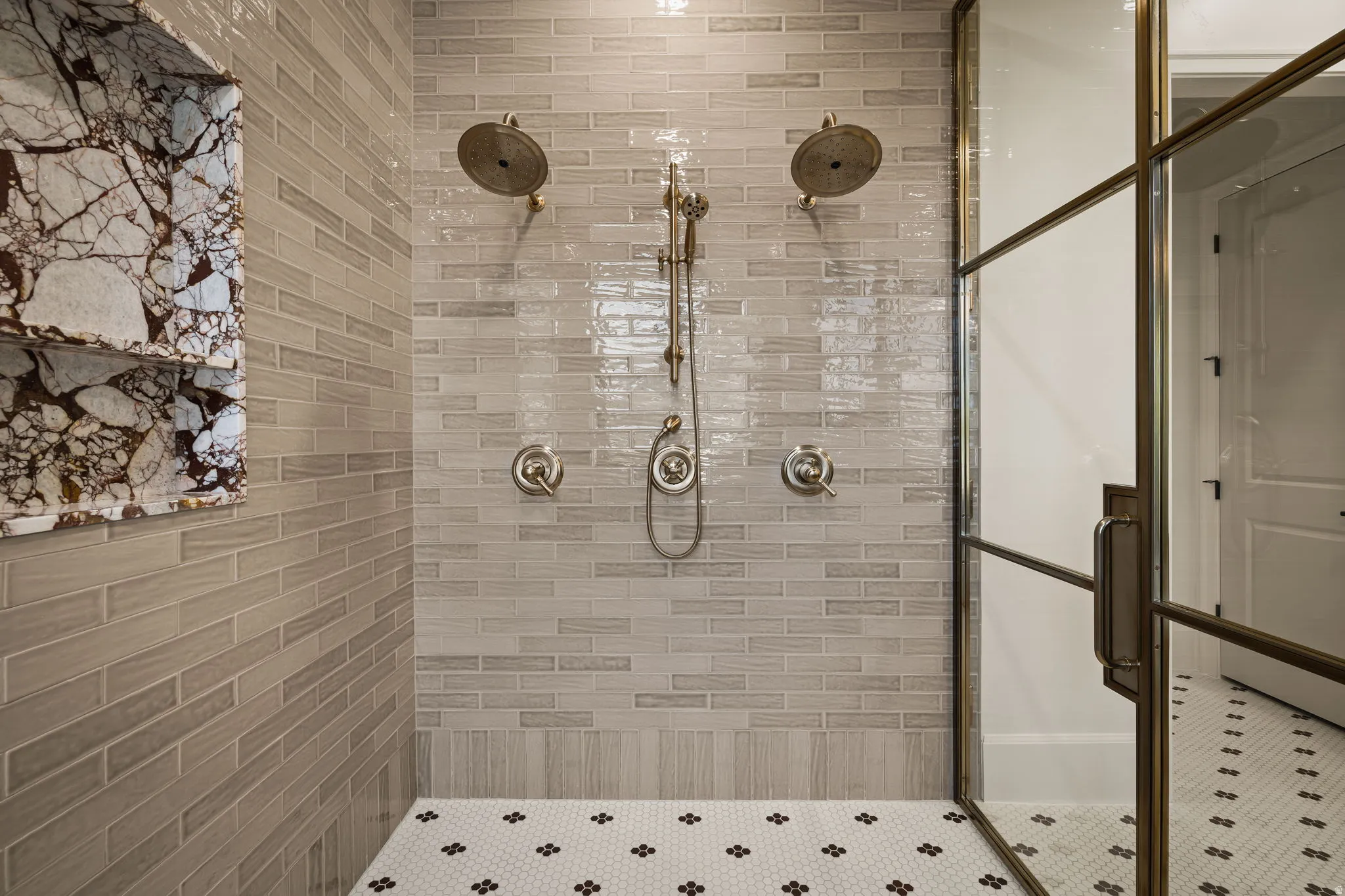 Walk-in shower featuring dual overhead showerheads, a handheld spray, and a built-in marble-finish niche