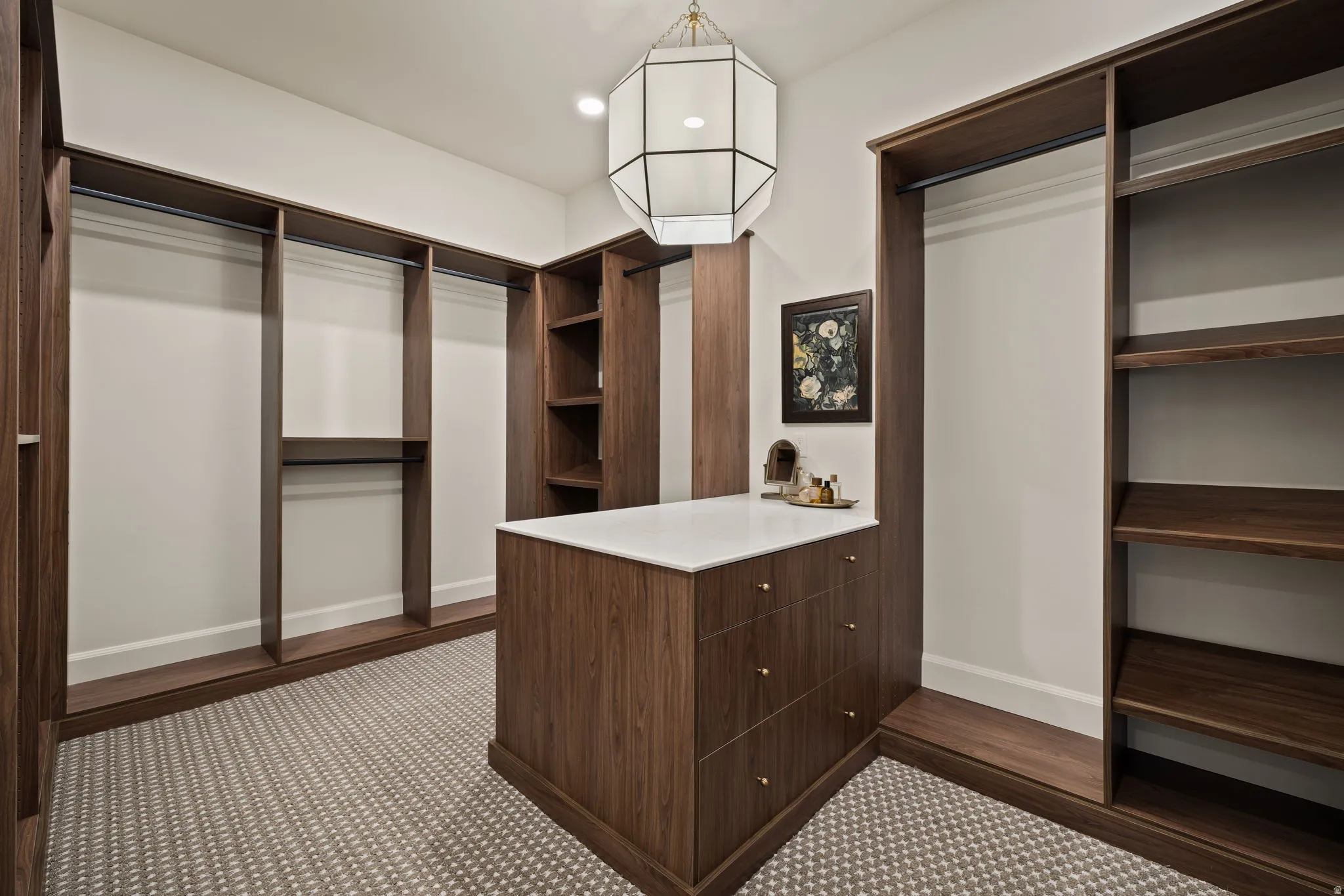 Custom walk-in closet featuring extensive dark wood-finish built-in shelving, hanging rods, and an island with white countertop and drawers