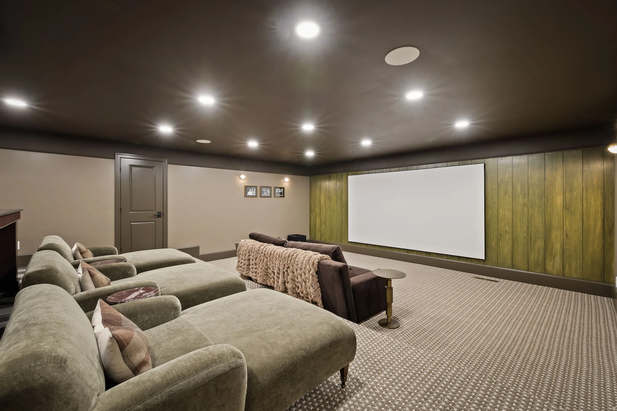 Dedicated media room featuring a large projector screen, recessed lighting, sound-absorbing ceiling panels, wood-paneled accent wall, and patterned carpeting