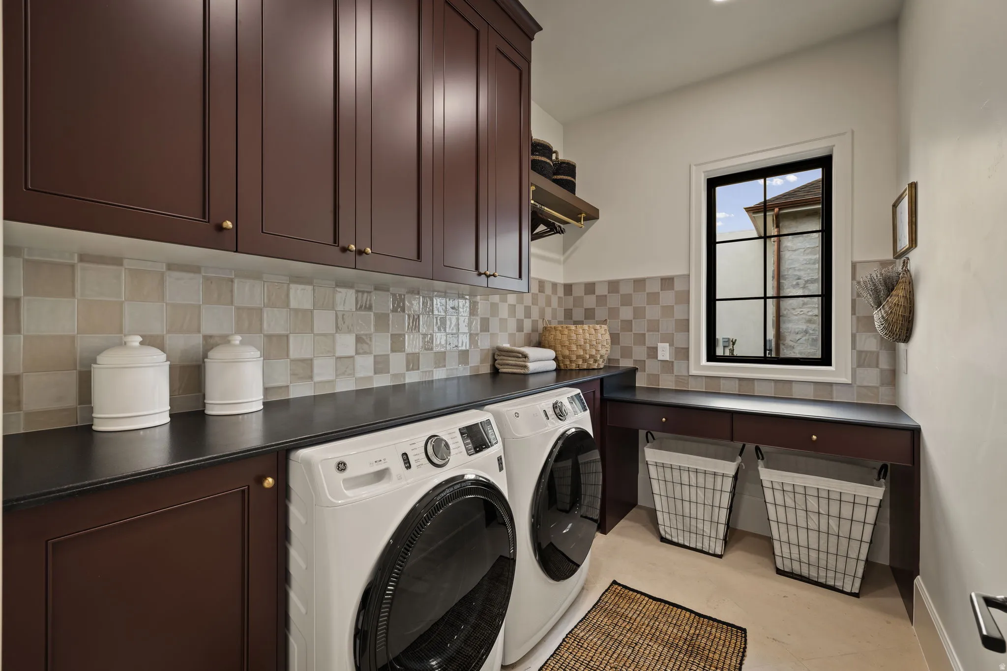 Laundry room featuring rich wood cabinetry, durable dark countertops, and a checkered tile backsplash