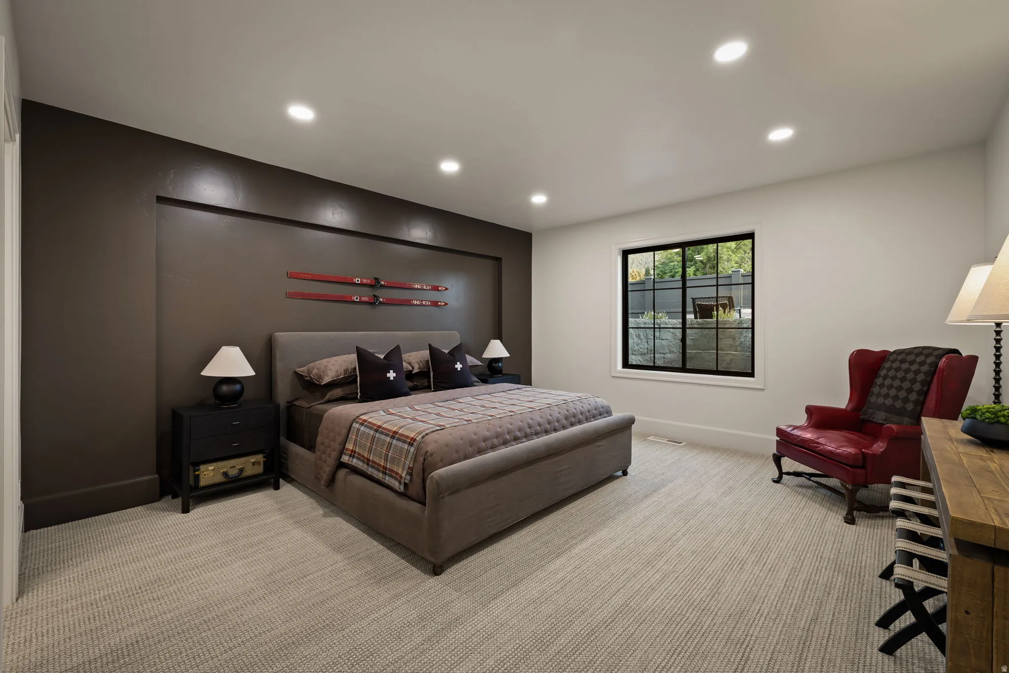 Spacious bedroom featuring textured carpeting, recessed lighting, a large black-framed window, and a distinct accent wall