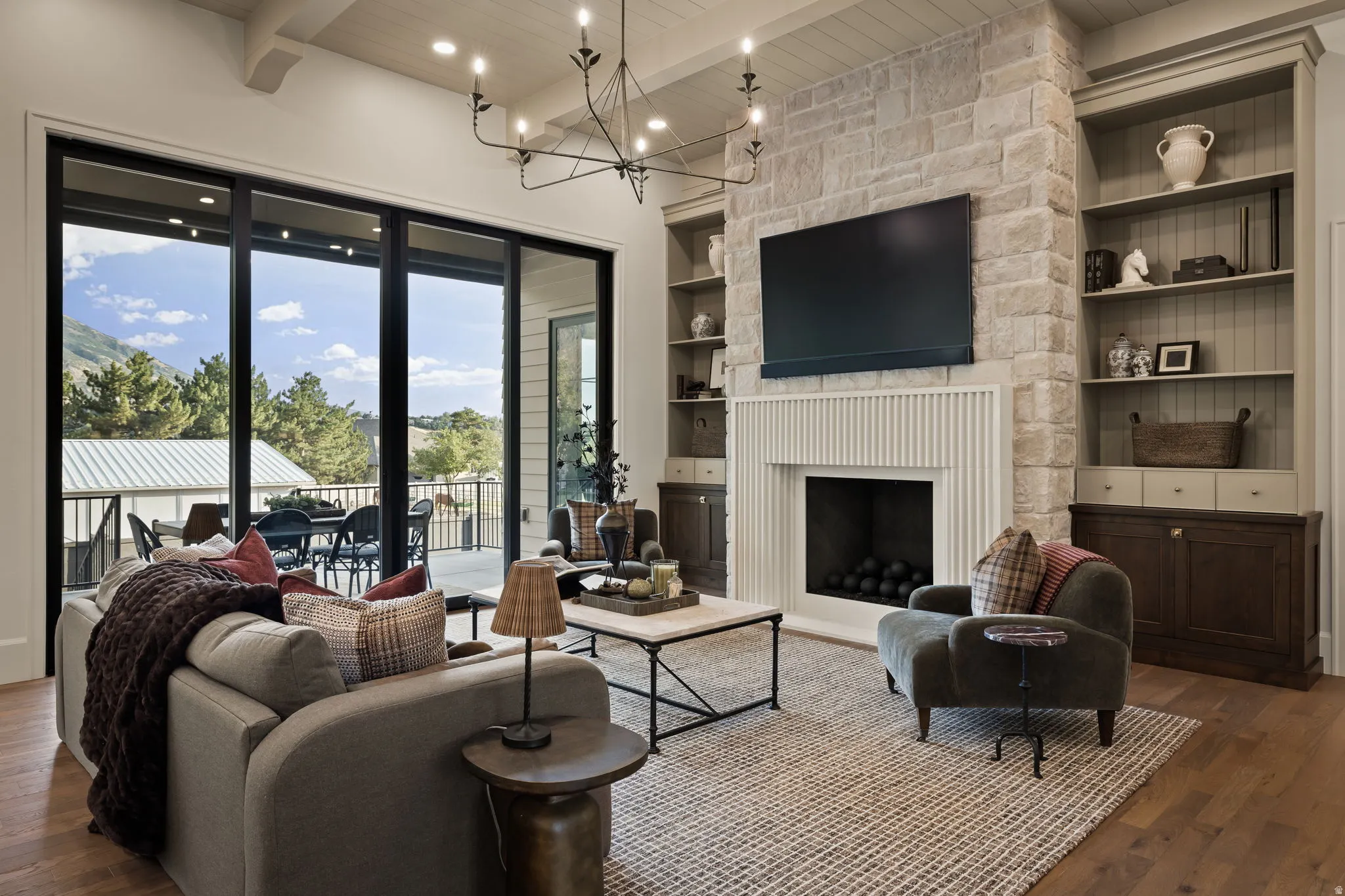 Spacious living area featuring expansive sliding glass doors, a stone fireplace with a fluted mantel, built-in shelving, wood-finish flooring, and a coffered ceiling
