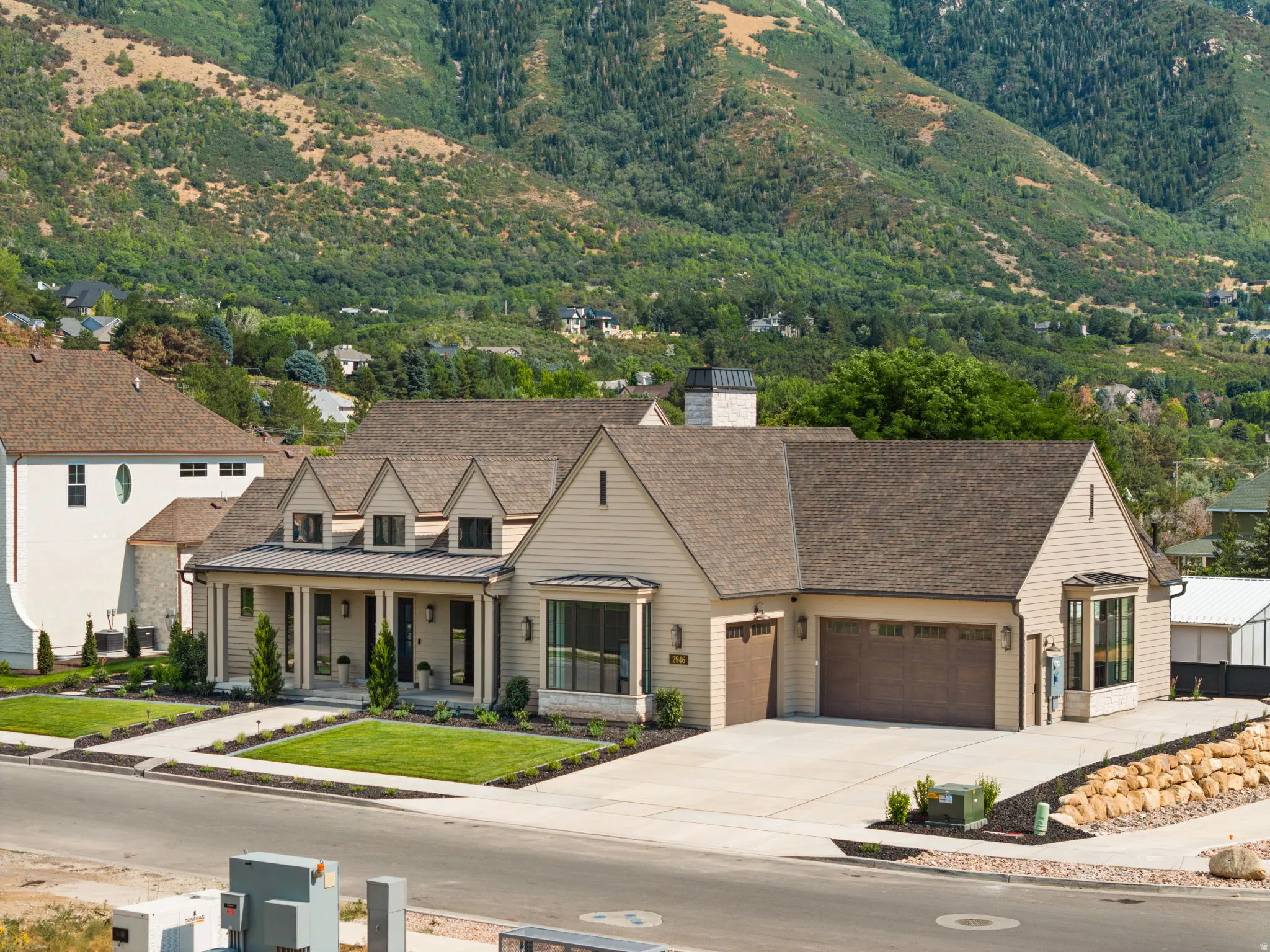 Contemporary home with a mountain backdrop, featuring a covered front porch, dual garage doors, and a stone-accented chimney