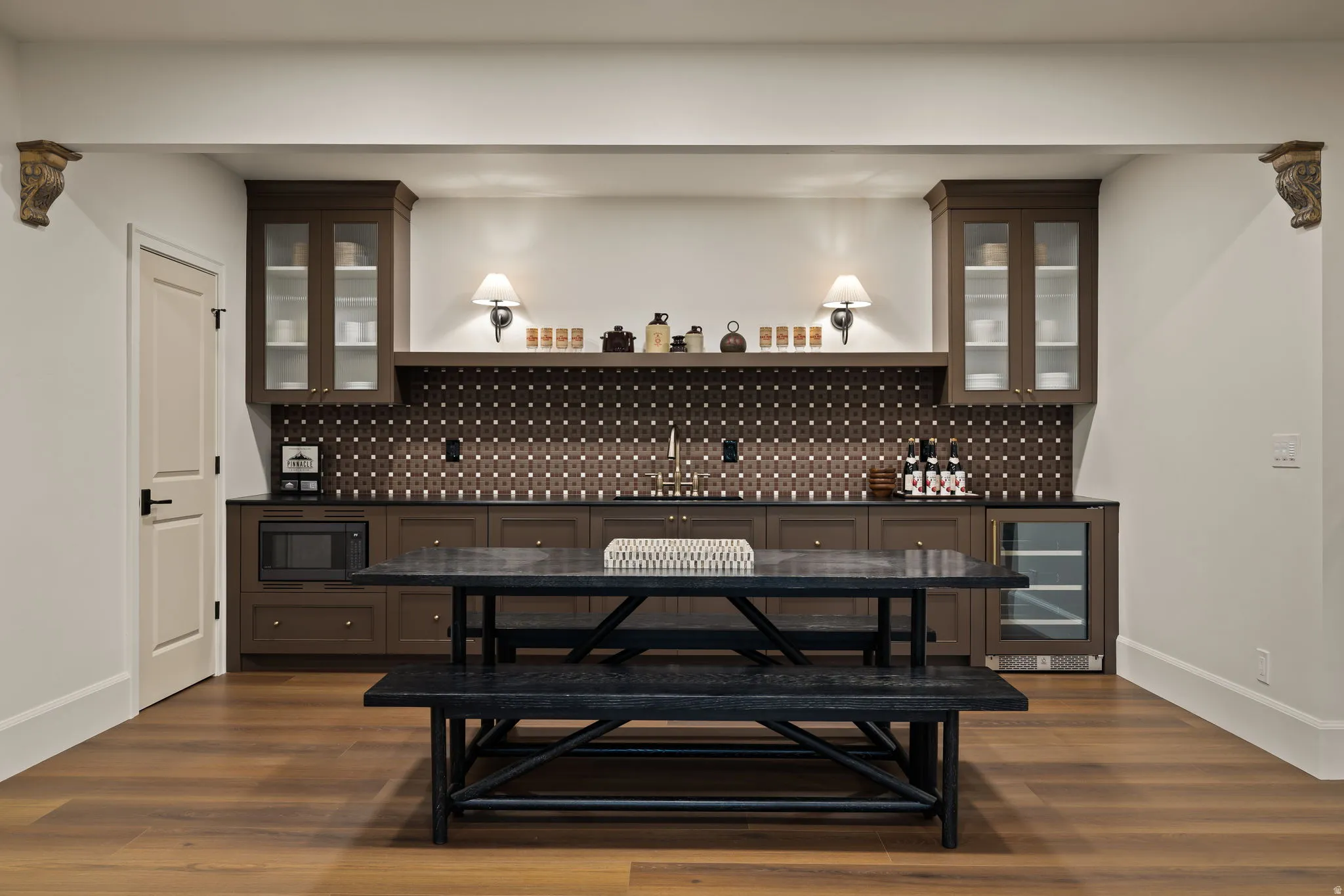Integrated wet bar featuring rich brown cabinetry, dark countertops, and a patterned tile backsplash